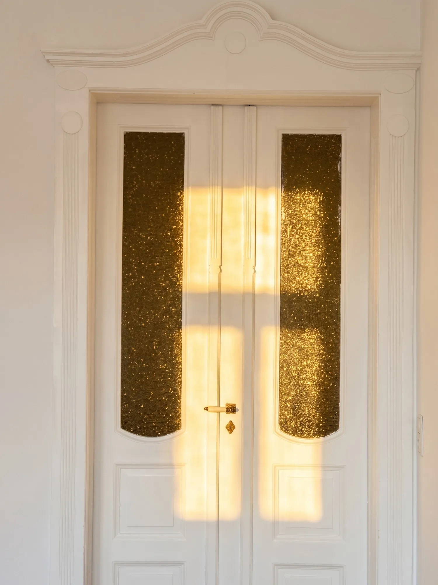 Weiße Flügeltür mit Goldglas im Abendlicht